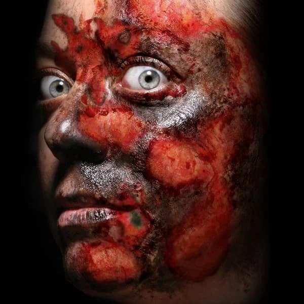 Face covered in red and scorched burn wound temporary tattoos, close-up on a black background